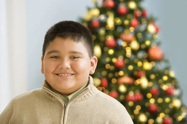 Hispanic boy smiling near Christmas tree