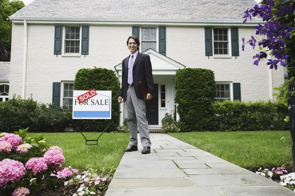 Male real estate agent and Sold sign in front of house