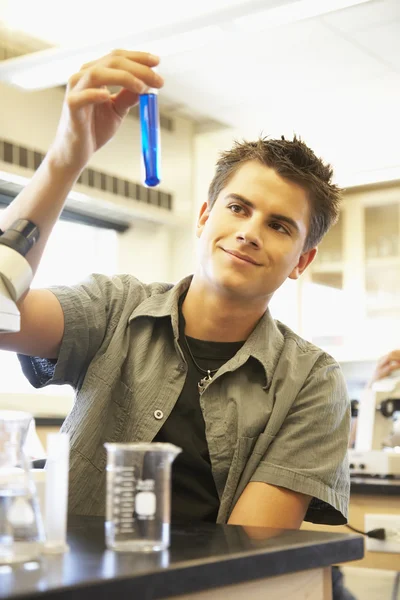 Teenaged boy with vial and beaker in science class