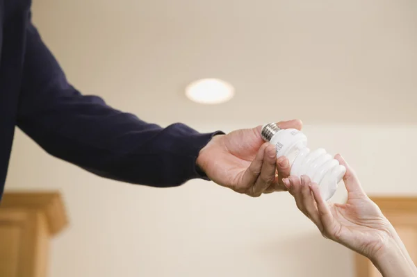 Hispanic man handing woman compact fluorescent light bulb