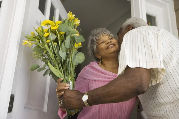 Senior African man giving flowers to wife in doorway