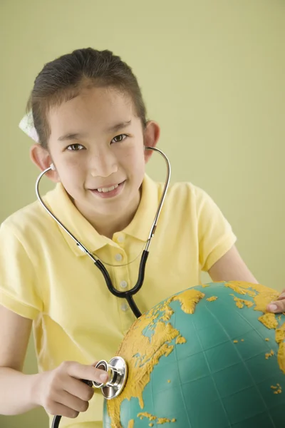 Asian girl holding stethoscope against globe