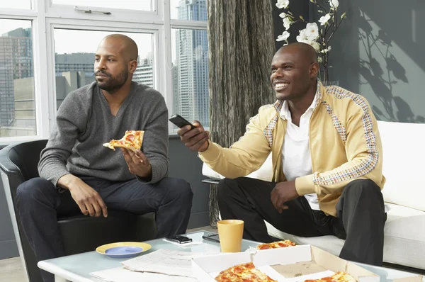 African men watching television and eating pizza in living room