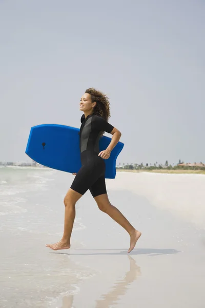 Mixed race woman running with boogie board at beach