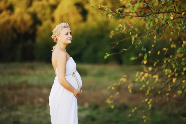 Beautiful pregnant young woman in greek white dress outside