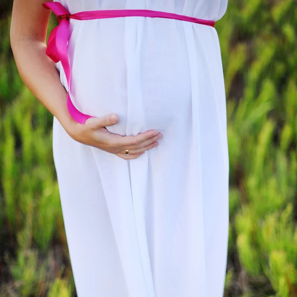 Young caucasian pregnant woman in a white greek dress