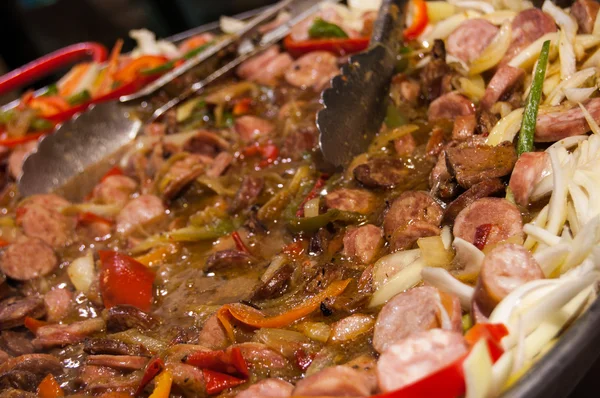 Hot stewed sausage and meat with vegetables in big pan at street market. Closeup. Raising steam. Christmas market in Paris.