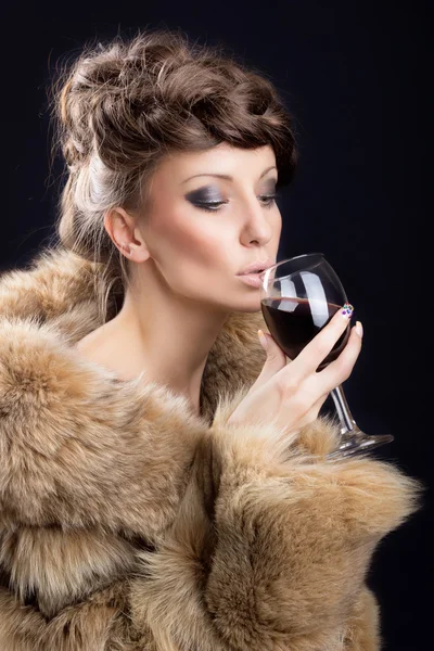 Gorgeous woman in luxurious fur drinking wine