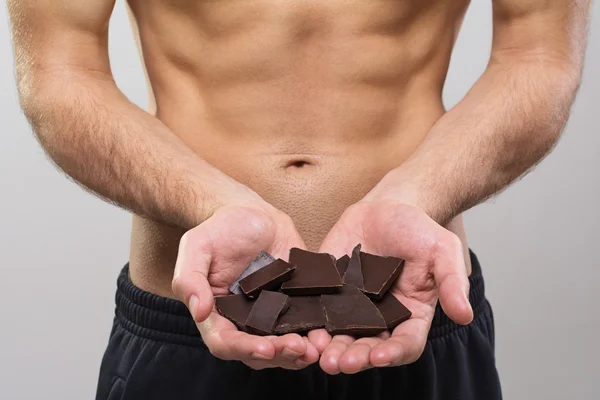 Young fit man holding dark chocolate pieces