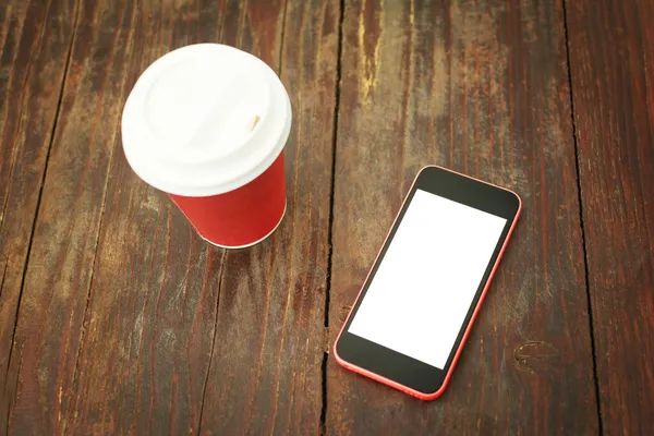 Smart phone and takeaway coffee cup on wooden table