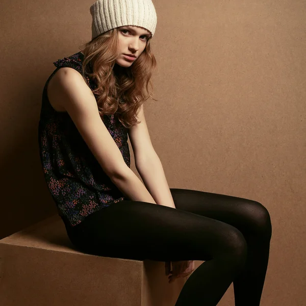Fashionable model with curly red hair and beige hat sitting on a