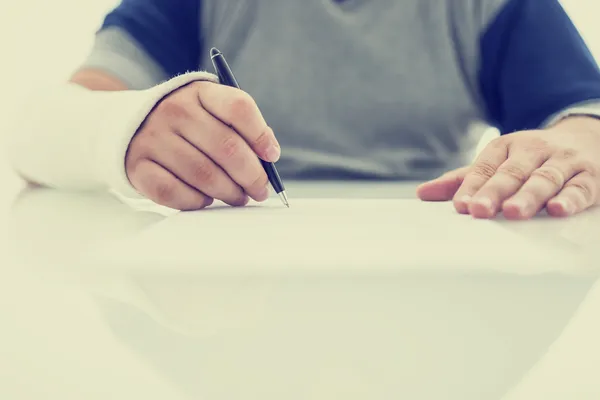 Man with his arm in a plaster cast writing