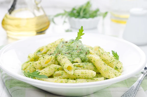 Pasta penne with sauce of arugula and green peas close-up