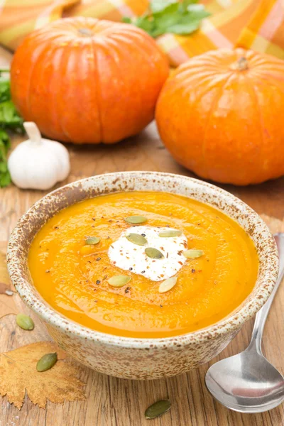 Pumpkin soup with coriander and cream on a wooden table