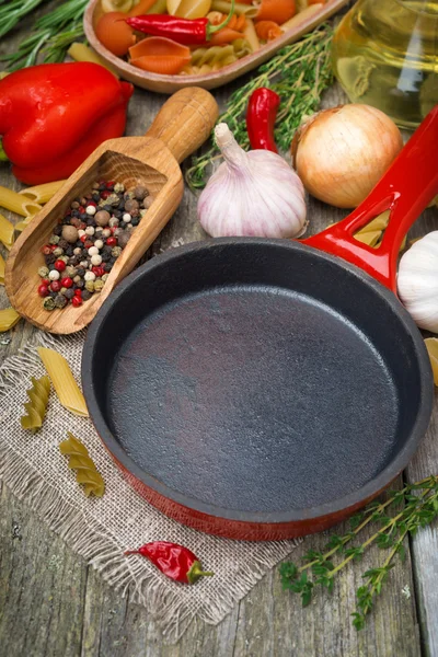 Empty frying pan, vegetables and spices on wooden background