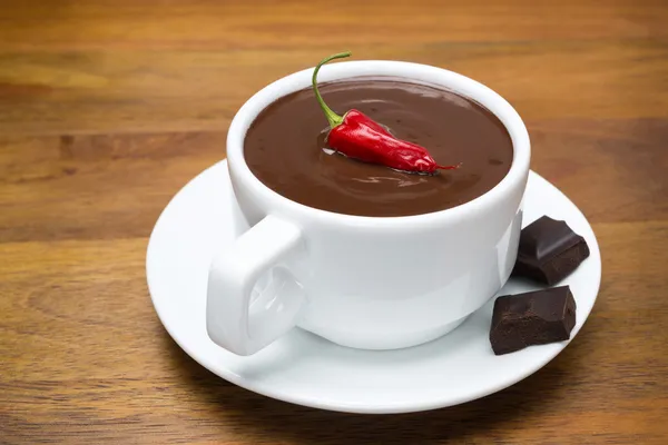 Cup of hot chocolate with chili peppers on a wooden background