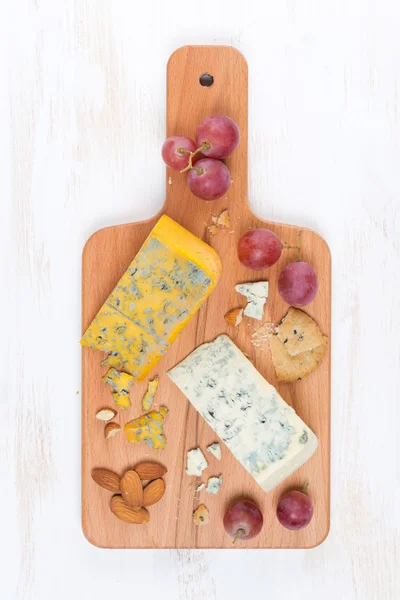Assorted soft cheeses, grapes, nuts on a wooden cutting board