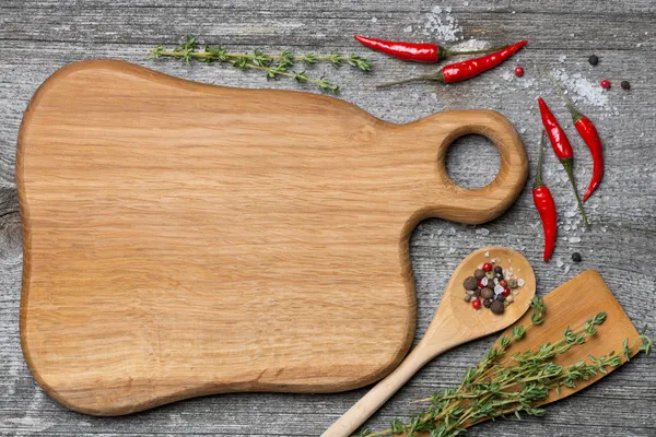 Figured wooden cutting board, spoon, spatula, herbs and spices