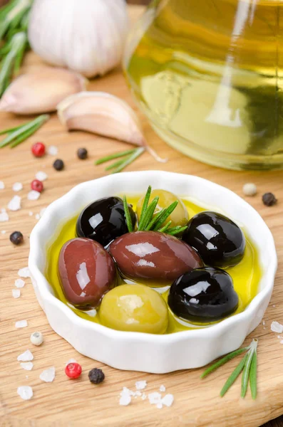 Three kinds of olives in a bowl with olive oil and spices