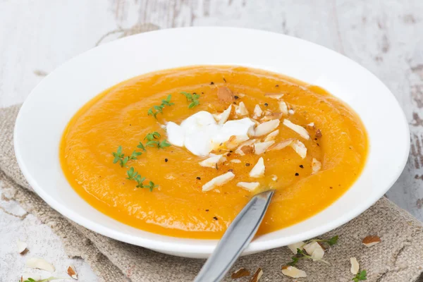 Carrot soup with almonds, yogurt and watercress on white wooden