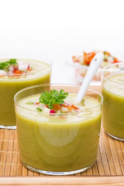 Green soup with fresh vegetables in glasses on wooden tray