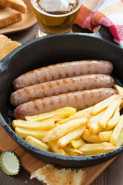 Grilled sausages with French fries in a frying pan, vertical