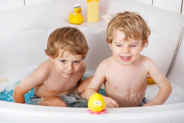 Two little twins boys having fun with water by taking bath in ba