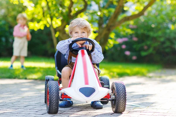 Two little sibling boys playing with pedal car in home's garden