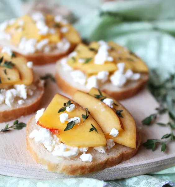 Wheat bread baguette bruschetta with salted greek feta cheese, fresh ripe nectarine slices, thyme and honey drizzling