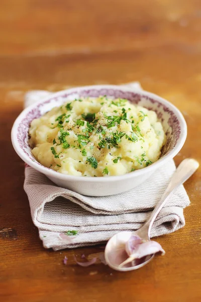 Portion of mashed potatoes with roasted garlic cloves, black pepper and fresh chopped parsley in a bowl with a spoon