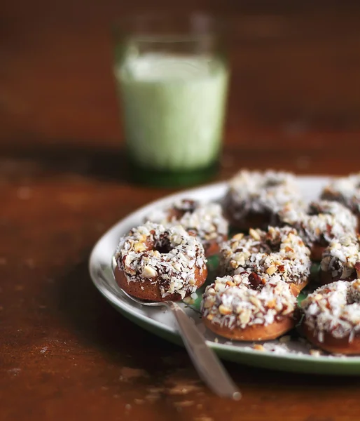 Homemade donuts with date spread, shredded coconut and toasted chopped nuts in a plate with a glass of fresh milk for healthy breakfast