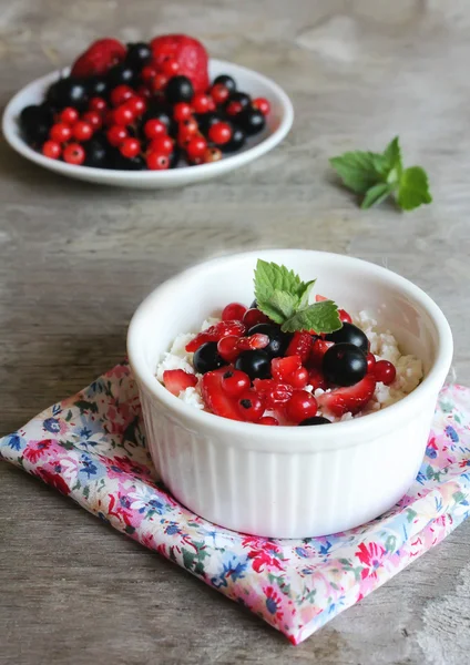 Healthy homemade crumbled cottage cheese with sour cream, honey, vanilla, fresh red and black currants, strawberry and mint leaves in a bowl for breakfast
