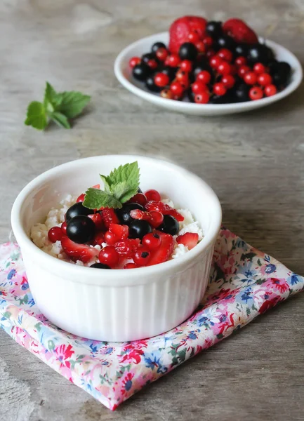 Healthy homemade crumbled cottage cheese with sour cream, honey, vanilla, fresh red and black currants, strawberry and mint leaves in a bowl for breakfast