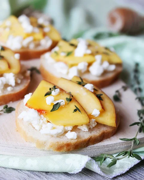 Homemade bruschetta with toasted wheat bread, ripe nectarines and peaches, crumbled feta cheese, dried thyme, honey in a wooden cutting board perfect for summer picnic snack, breakfast, appetizer