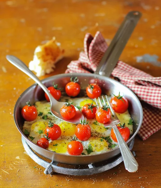 Fried quail eggs with roasted cherry tomatoes, mozzarella cheese, fresh chopped parsley, ground black pepper and a slice of homemade ciabatta in a frying pan for morning breakfast or lunch