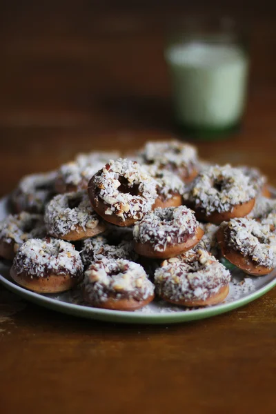 Homemade donuts with chocolate, cocoa, fig spread, chopped hazelnuts and freshly shredded coconut in a plate and a glass of fresh milk for breakfast