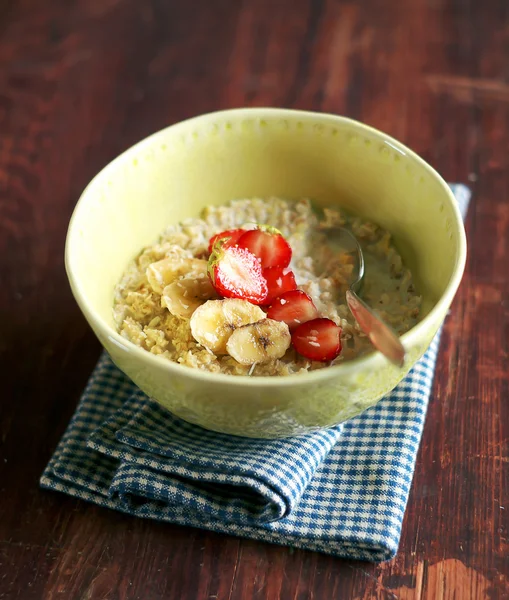 Bowl of oatmeal porridge served with fresh chopped strawberry, banana slices and freshly shredded coconut for morning breakfast or healthy snack, selective focus