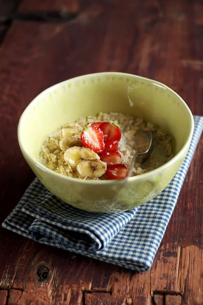 Bowl of oatmeal porridge served with fresh chopped strawberry, banana slices and freshly shredded coconut for morning breakfast or healthy snack, selective focus