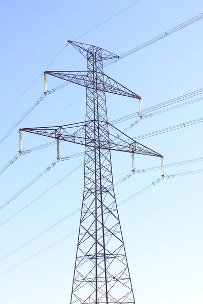 High voltage power tower and electrical lines against blue sky.