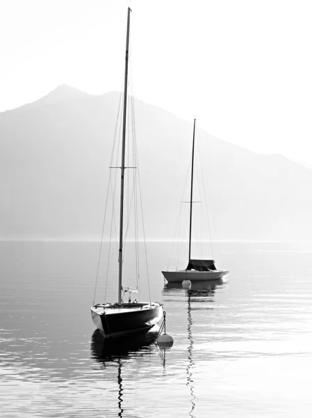 Two sail boats in early morning on the mountain lake. Black and white photography. Salzkammergut, Austria.