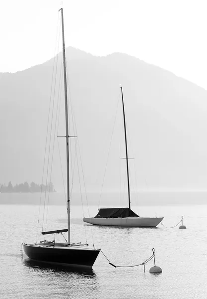 Two sail boats in early morning on the mountain lake. Black and white photography. Salzkammergut, Austria.