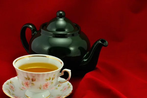 A cup of tea and green teapot on a red background