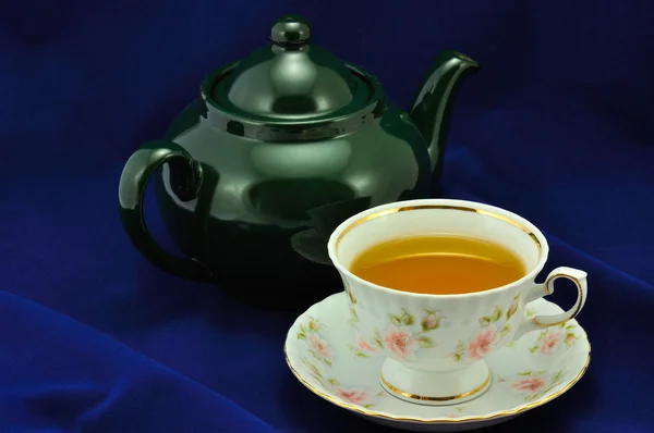 A cup of tea and green teapot on a blue background