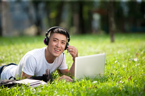 Young handsome asian student using laptop in the park