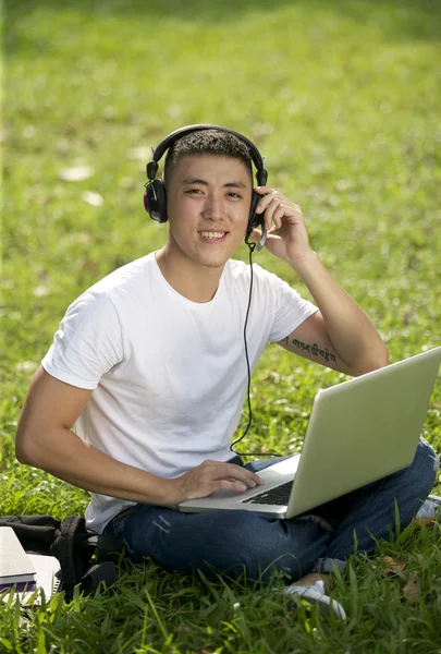Young handsome Asian student with laptop and headset out door — Stock Photo #21584803