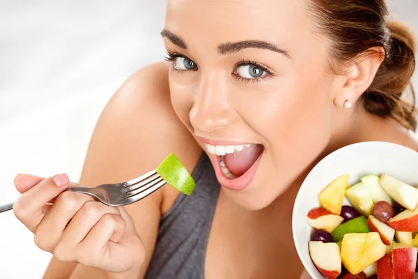 Slim young woman eating fruit salad