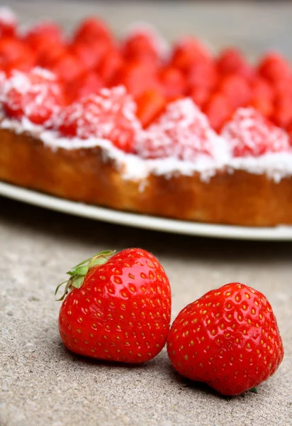 A pair of strawberries on the floor with a strawberry cake in the background