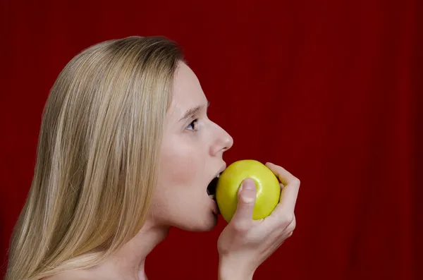 Young blonde biting on apple on red background