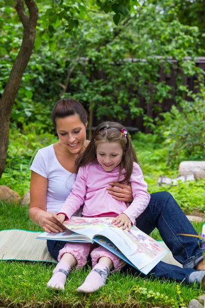 Mother and daughter read book outdoors