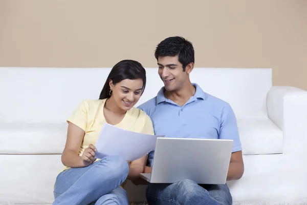 Woman holding paper while man using laptop